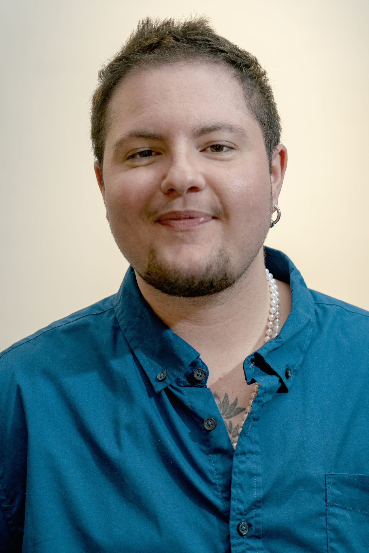 Smiling man with black glasses wearing a black polo shirt, tattoos visible, against a solid red background.